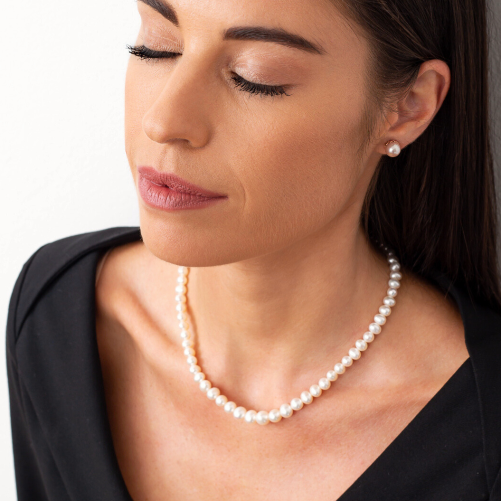 Žena s uzavřenýma očima nosí elegantní perlový náhrdelník s kulatými bílými perlami a ladícími perlovými náušnicemi.